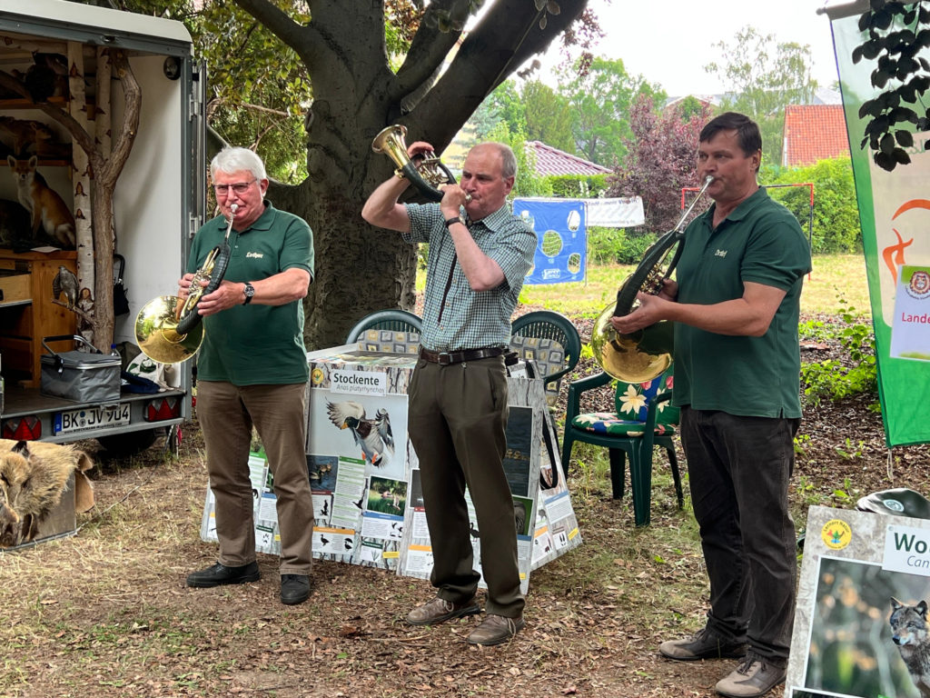 Drei Männer spielen verschiedene Blasinstrumente.